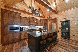 A spacious kitchen with wooden cabinetry, a central island with bar stools, and a stainless steel refrigerator. - Misty Mountain Luxury mountain cabin with breathtaking views, hot tub, & game room! (Murphy)