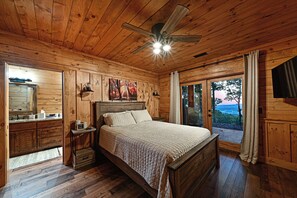 A wooden cabin bedroom with a bed, a nightstand, a mirror, and a ceiling fan. - Misty Mountain Luxury mountain cabin with breathtaking views, hot tub, & game room! (Murphy)