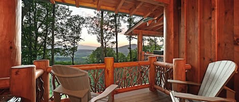 Una terraza de madera con sillas Adirondack y vistas a un paisaje montañoso.