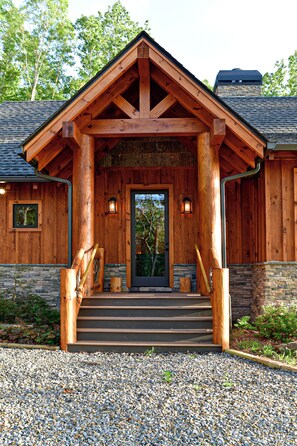 A wooden lodge with a stone foundation, a front porch with steps, and a door with a glass panel. - Misty Mountain Luxury mountain cabin with breathtaking views, hot tub, & game room! (Murphy)