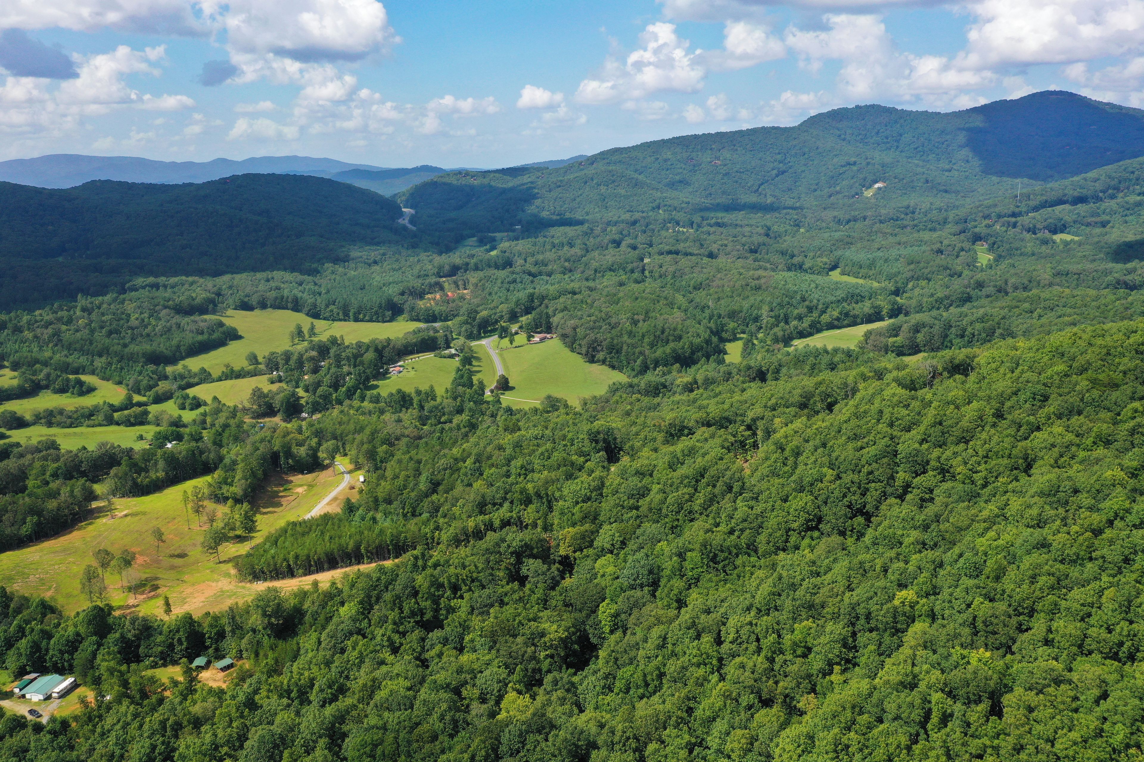 Eine ländliche Landschaft mit sanften Hügeln, dichten Wäldern und vereinzelten Gebäuden.