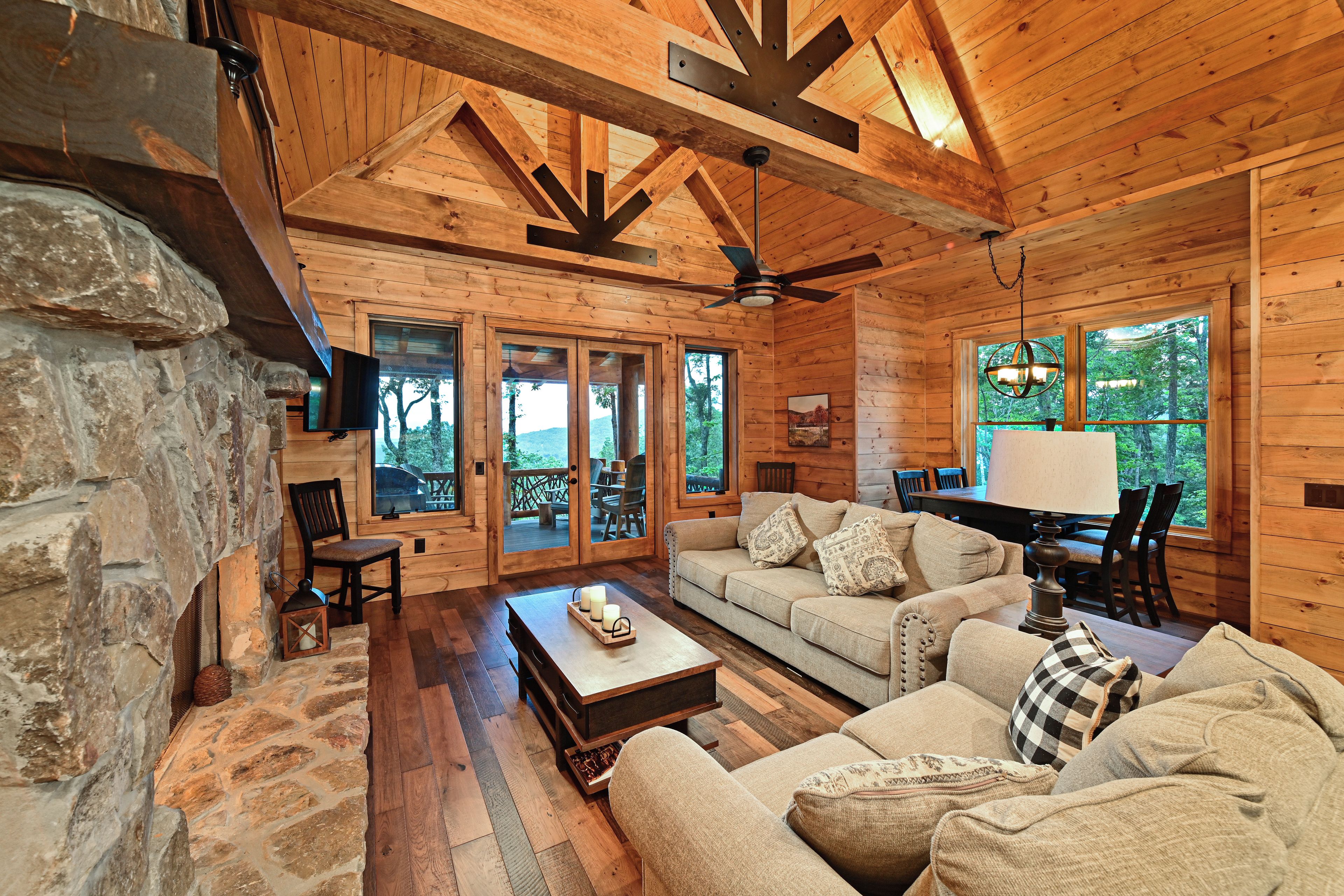 A log cabin interior with a stone fireplace, wooden flooring, a sofa set, and a dining area.