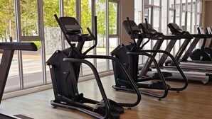 Une salle de sport équipée de tapis de course, de vélos d’exercice et d’un banc de musculation.