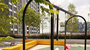 Un terrain de jeux avec des balançoires et un banc jaune, entouré d’arbres et d’immeubles.