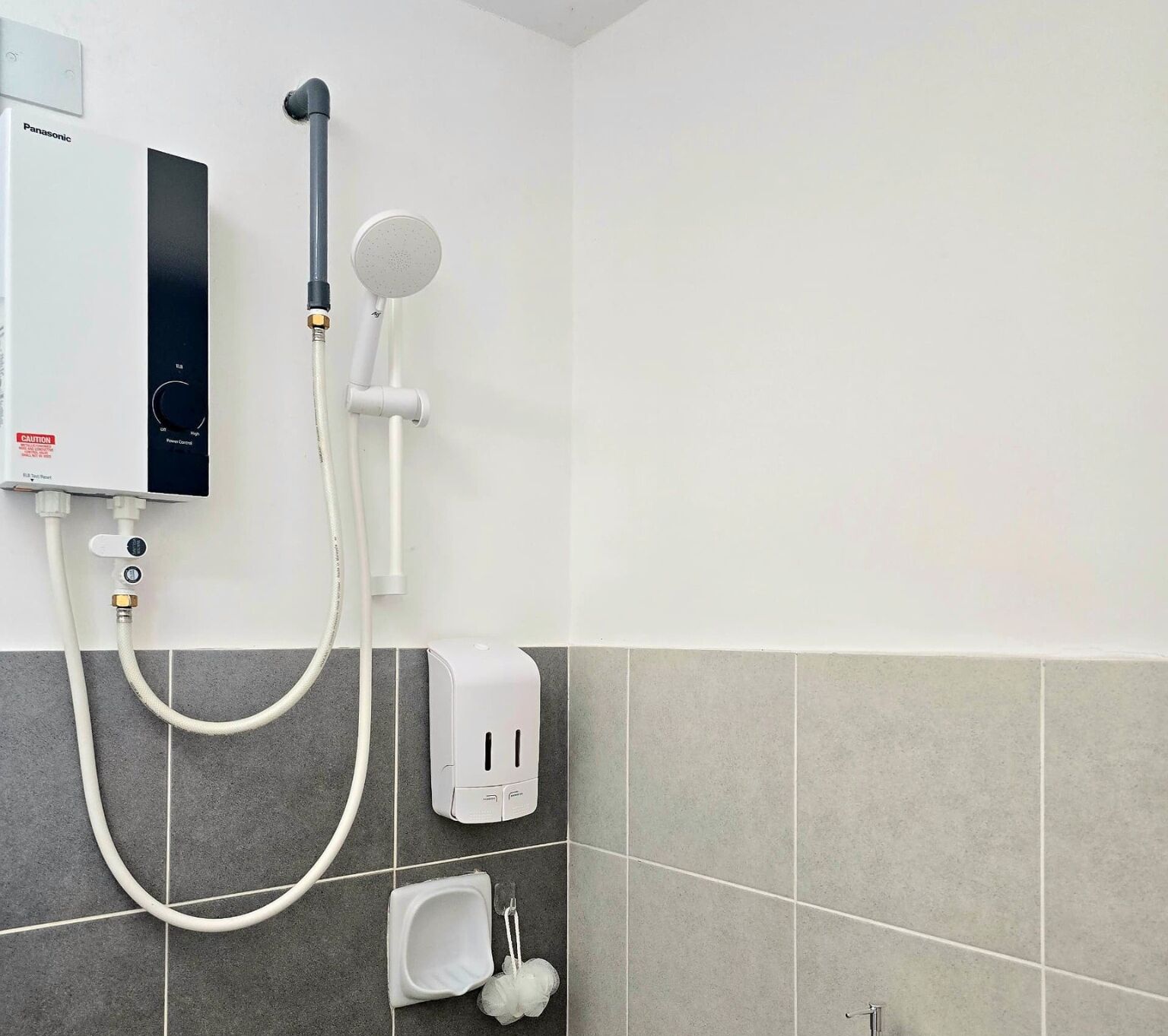 Um banheiro com vaso sanitário branco, dispensador de sabonete e chuveiro manual fixado na parede.