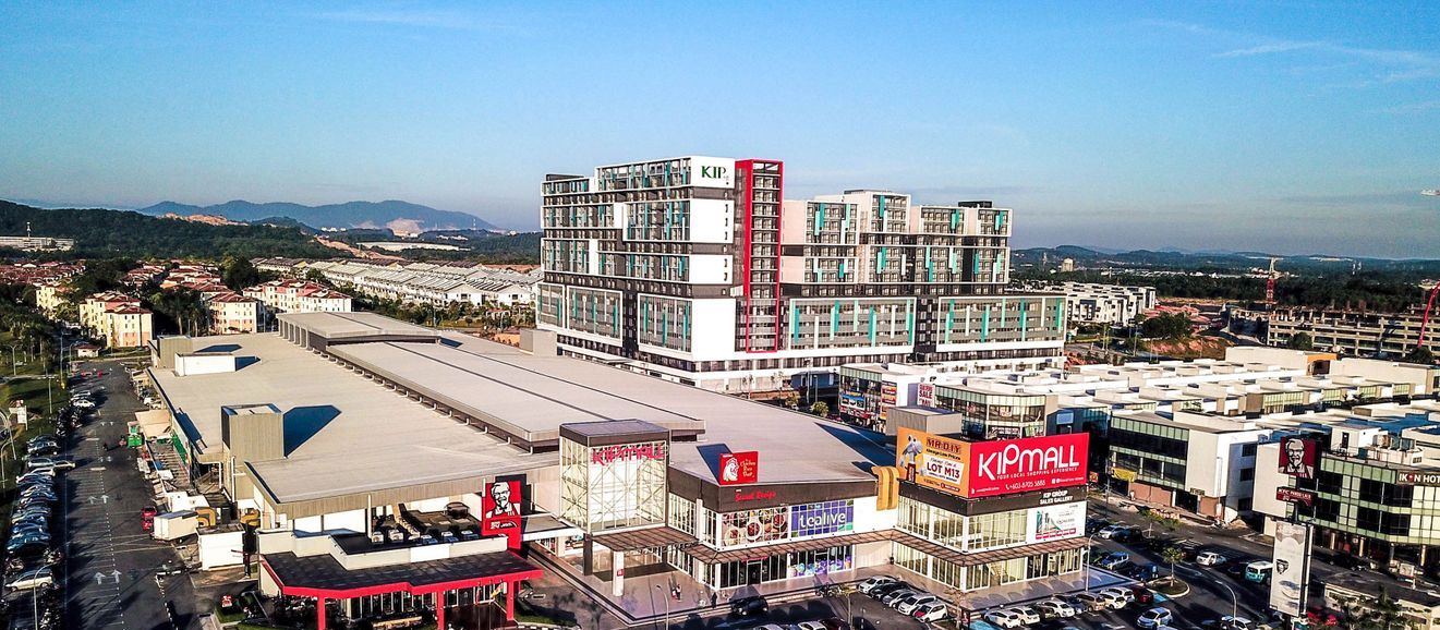 Zona comercial con una destacada tienda KIPMALL, una gasolinera y un edificio grande de varios pisos con detalles en rojo.