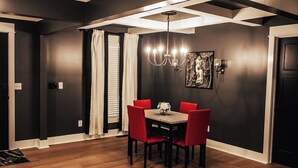 Un comedor con mesa de madera y sillas rojas, una araña y un cuadro en la pared.