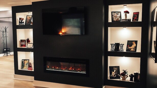 Una sala de estar moderna con chimenea, un televisor de pantalla plana y estanterías con libros y adornos.