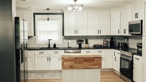 Una cocina moderna con gabinetes blancos, una isla central, un microondas y una estación de café.
