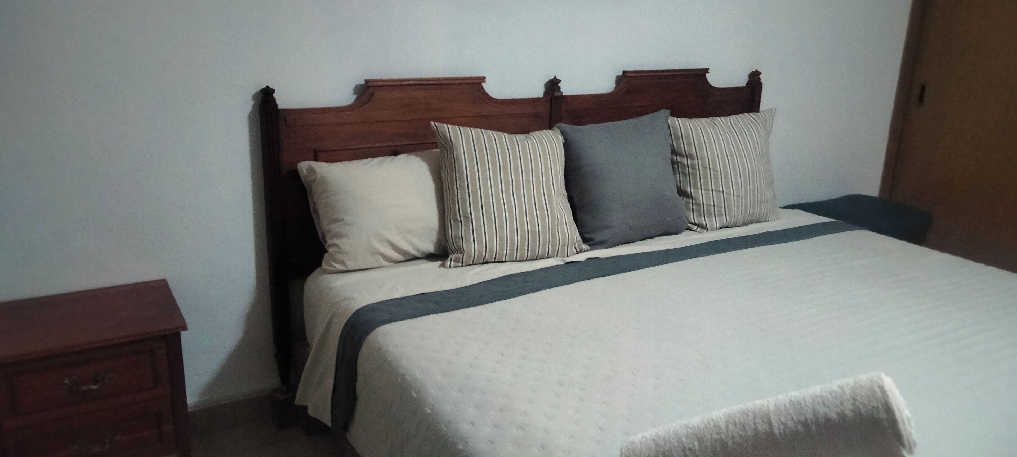 A bed with a wooden headboard, a white bedspread, and striped pillows.