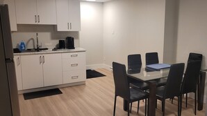 A compact living space with a kitchenette, a dining area with a glass table and black chairs, and a grey sofa with a patterned cushion.
