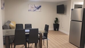 A modern kitchen with a dining area, a refrigerator, and a flat-screen TV mounted on the wall.