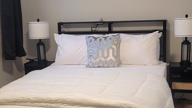 A neatly made bed with white bedding, a black headboard, and two bedside lamps.
