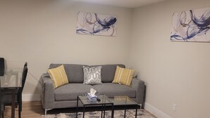 A living room with a gray sofa, two yellow pillows, a glass coffee table, and abstract wall art.