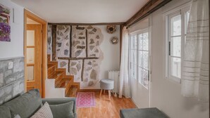 Una sala de estar acogedora con una pared de piedra, una escalera de madera, un sofá gris y una ventana con cortinas.