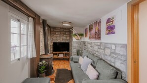 Una sala de estar acogedora con una pared de piedra, un sofá gris, un televisor de pantalla plana y piso de madera.