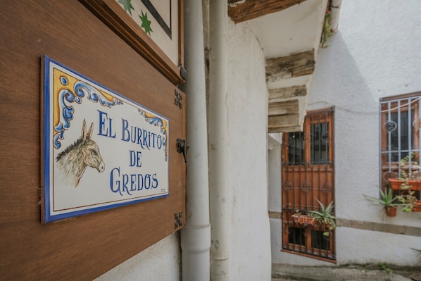 Une enseigne illustrée d’un cheval et portant un texte, fixée à un bâtiment aux murs blancs et aux poutres en bois.