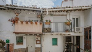 Un edificio de dos pisos con balcón, plantas en macetas y una ventana pequeña.