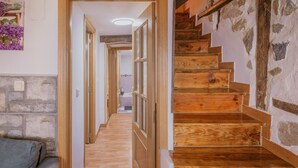 Un pasillo con piso de madera, pared de piedra y escalera de madera.