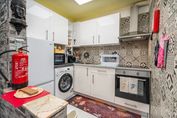 A modern kitchen with a washing machine, oven, and patterned backsplash.