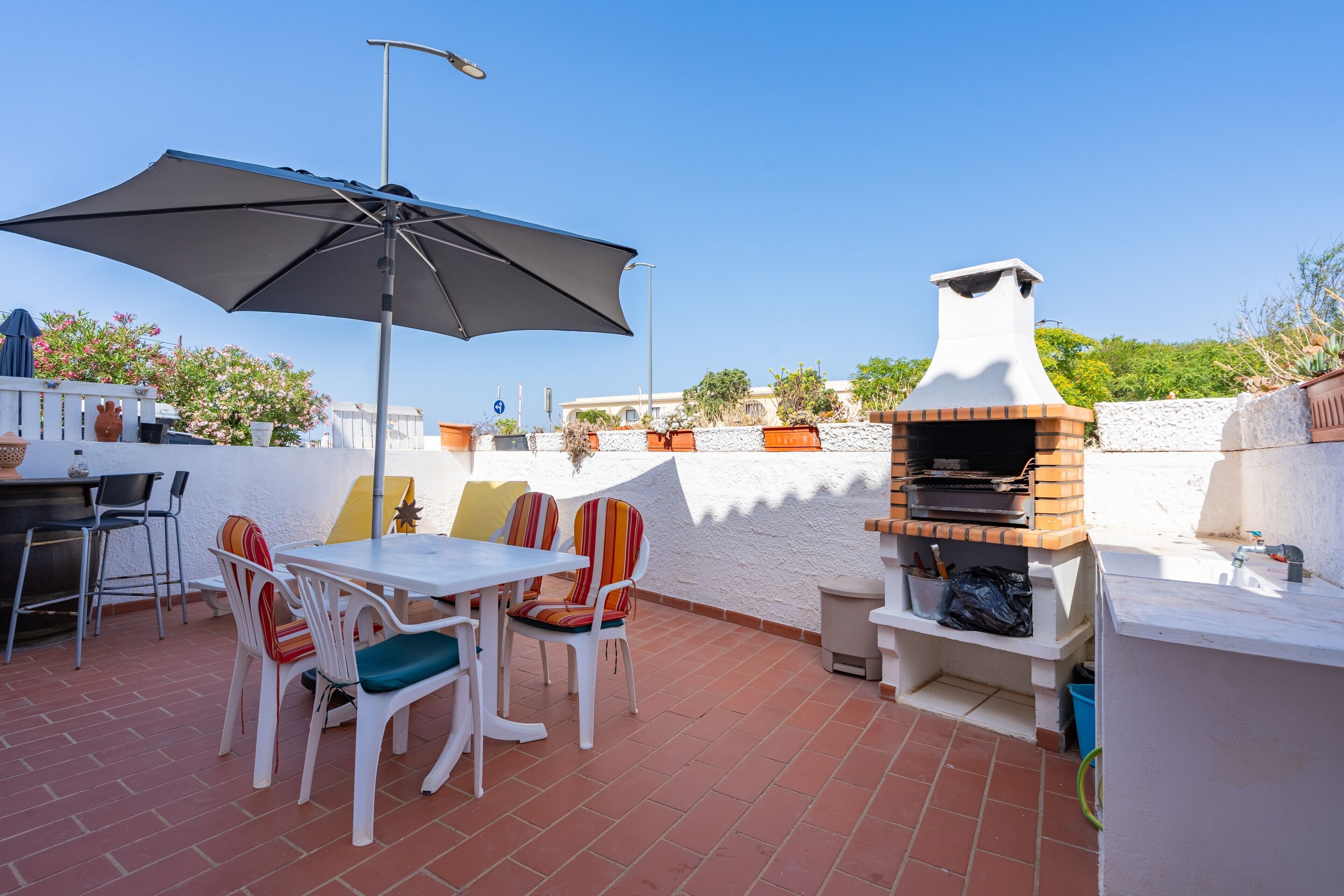 An outdoor patio with a brick oven, white table, chairs, and an umbrella.