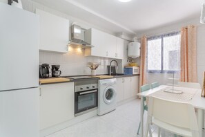 A modern kitchen with white cabinets, a built-in oven, a washing machine, and a dining area with a table and chairs. - Retama Vacation Apartment with Sea Views, Balcony and Wi-Fi (Adeje)