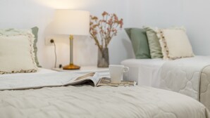 Un lit bien fait, avec une tasse et un livre, une lampe de chevet et un vase contenant des fleurs séchées.