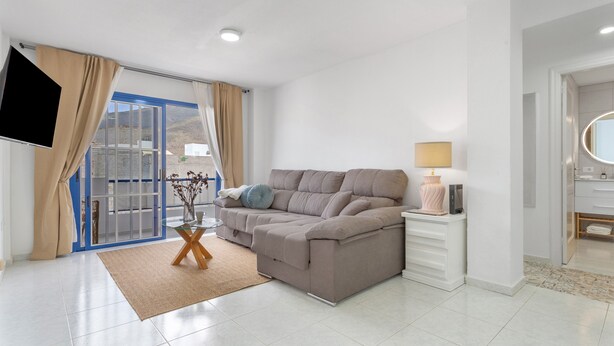 Un salon moderne avec un canapé, un téléviseur, une lampe et une vue à travers une porte vitrée.