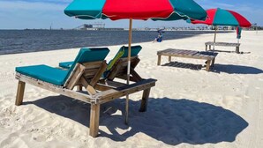 A beach with wooden lounge chairs and red and blue umbrellas. - Family Getaway with Huge Private Yard • 5 min to Beach • Peaceful Are (Gulfport)