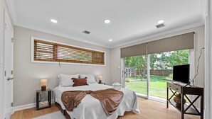 A bedroom with a large bed, bedside tables, a TV, and a view of the outdoors. - Family Getaway with Huge Private Yard • 5 min to Beach • Peaceful Are (Gulfport)