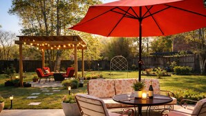 An outdoor patio with a round table, red chairs, a red umbrella, and a wooden pergola with string lights. - Family Getaway with Huge Private Yard • 5 min to Beach • Peaceful Are (Gulfport)