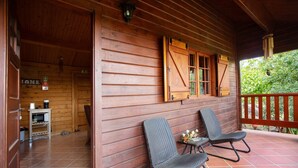 A wooden cabin with two rocking chairs on a porch, a small table with a vase, and a sign indicating the room number.