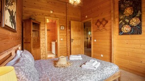 A wooden cabin bedroom with a bed, a hat, towels, a lamp, and a painting.
