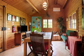 A wooden cabin interior with a dining table, chairs, a television, and a painting on the wall.