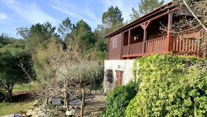 A rustic wooden building with a balcony, surrounded by greenery and trees.