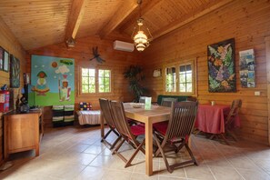 A wooden cabin interior with a dining table, chairs, a chandelier, and a mural on the wall.