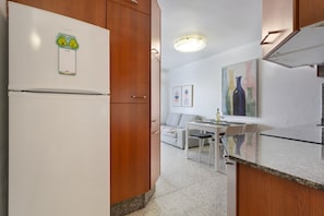 A kitchen with wooden cabinets, a white refrigerator, a dining table with chairs, and a painting on the wall. - Fabi Vacation Apartment with Private Terrace near the Beach (Arrieta)