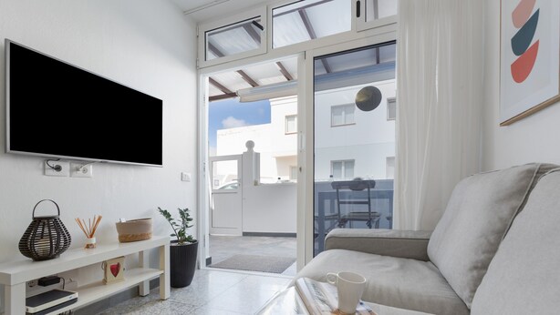 Un saló modern amb televisió plana, un sofà, una taula de centre amb una revista, una estanteria amb objectes decoratius, i vista a l'exterior.