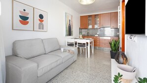 Un saló modern amb un sofà, una taula de dinar amb caires i una cuina amb armaris i encimera.
