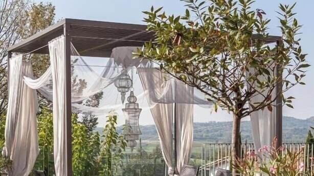 Un espace extérieur aménagé, abrité et doté de sièges confortables, ainsi qu’une pergola agrémentée de rideaux blancs.