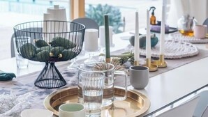 Une salle à manger bien éclairée, offrant une vue sur l’extérieur, avec une table dressée et agrémentée de différents plats, de verres et d’un centre de table décoratif.