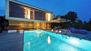 Une maison moderne à deux étages, dotée d’une piscine et d’une terrasse.