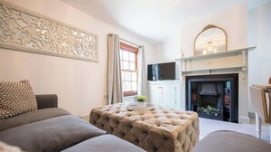 Ein Wohnzimmer mit Sofa, Ottoman, Kamin, Fernseher und Wanddeko.