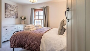 Ein Schlafzimmer mit Bett, Schminktisch, einem Gemälde und einem Fenster mit Vorhängen.