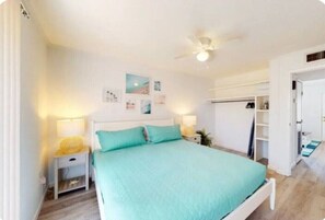Cozy retreat with a single bed, nightstand, and ceiling fan, featuring framed artwork and a shelf with a lamp.