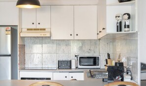 A modern kitchen with white cabinets, a microwave, a toaster, and a hanging light fixture. - KozyGuru | Balmain |  2BTownhouse bridge view (Balmain)