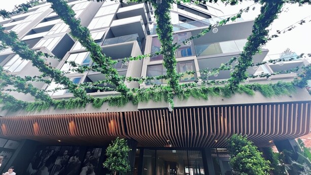 Un edificio moderno con una fachada geométrica singular, cubierto de vegetación y con una entrada de listones de madera.