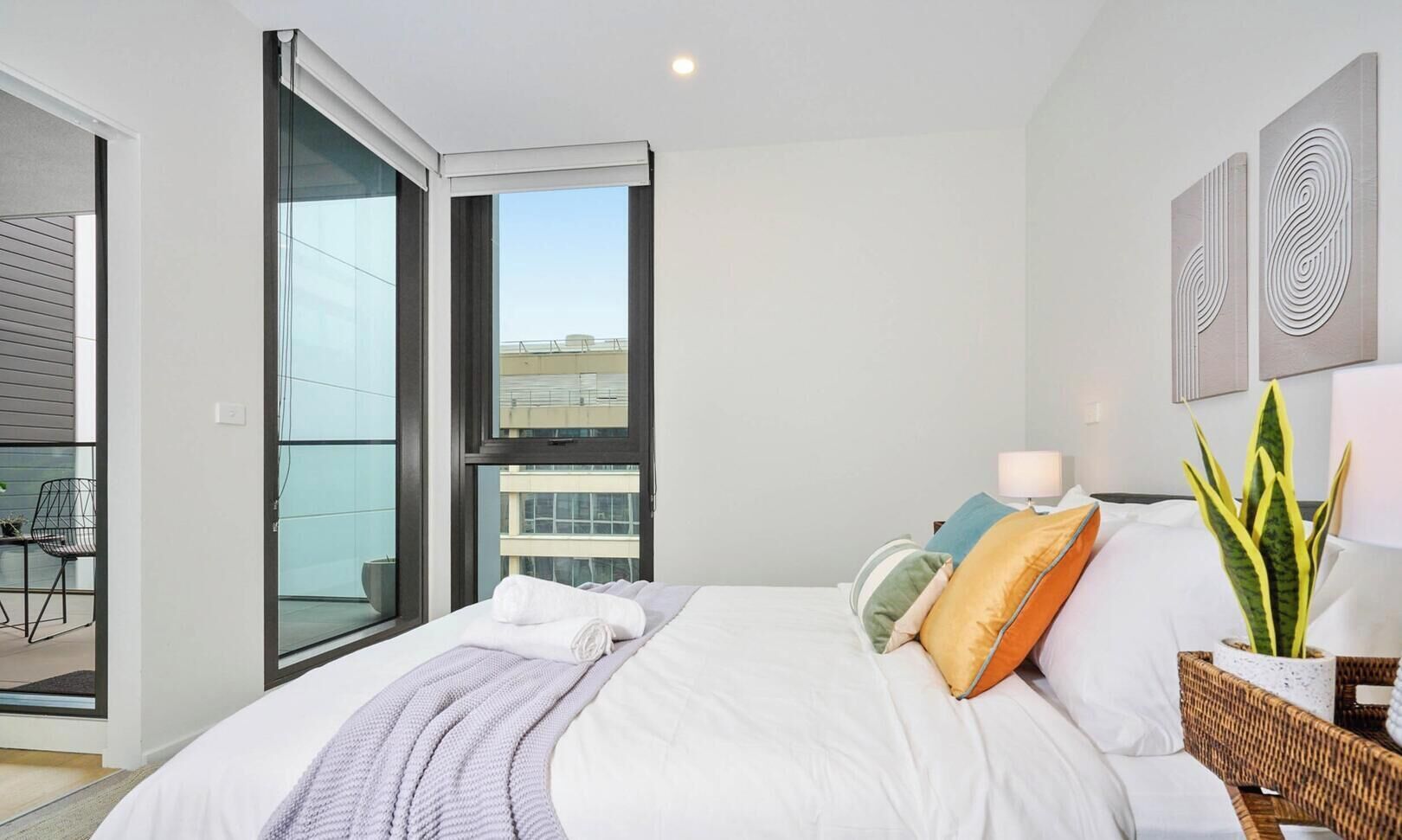 A modern bedroom with a large bed, a balcony, and a view of buildings.