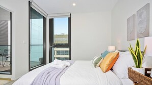 Un dormitorio moderno con una cama grande, un balcón y vistas a edificios.
