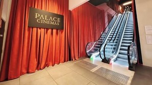 Una escalera mecánica conduce a un cine con cortinas rojas y un letrero que dice "PALACE CINEMAS".